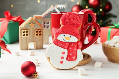 Photo of Delicious cookie in shape of snowman, cup with cocoa and Christmas decor on white wooden table, closeup