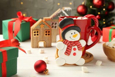 Photo of Delicious cookie in shape of snowman, cup with cocoa and Christmas decor on white wooden table