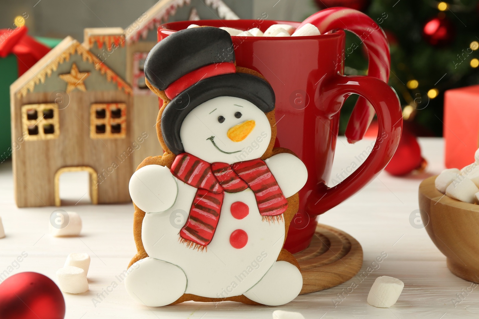 Photo of Delicious cookie in shape of snowman, cup with cocoa and Christmas decor on white wooden table, closeup