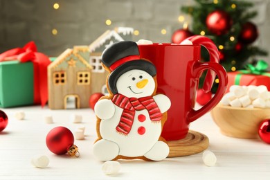 Photo of Delicious cookie in shape of snowman, cup with cocoa and Christmas decor on white wooden table