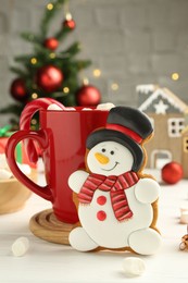 Photo of Delicious cookie in shape of snowman, cup with cocoa and Christmas decor on white wooden table