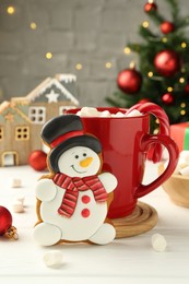 Photo of Delicious cookie in shape of snowman, cup with cocoa and Christmas decor on white wooden table