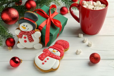 Photo of Delicious cookies in shape of snowmen, cup with cocoa and Christmas decor on white wooden table