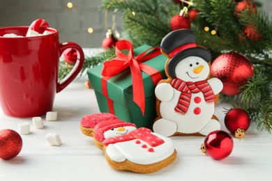 Photo of Delicious cookies in shape of snowmen, cup with cocoa and Christmas decor on white wooden table