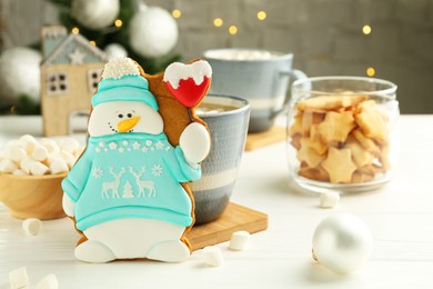 Photo of Delicious cookie in shape of snowman, cup with cocoa and Christmas decor on white wooden table