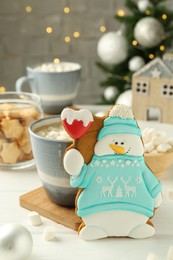 Photo of Delicious cookie in shape of snowman, cup with cocoa and Christmas decor on white wooden table