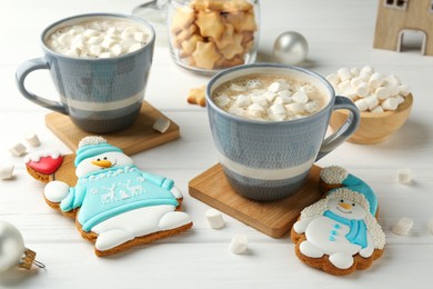 Photo of Delicious cookies in shape of snowmen, cups with cocoa and Christmas decor on white wooden table