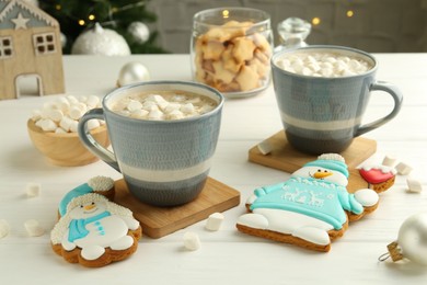 Photo of Delicious cookies in shape of snowmen, cups with cocoa and Christmas decor on white wooden table