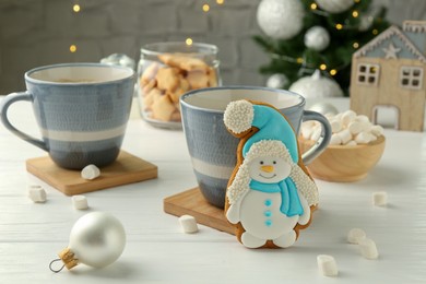 Photo of Delicious cookie in shape of snowman, cups with cocoa and Christmas decor on white wooden table