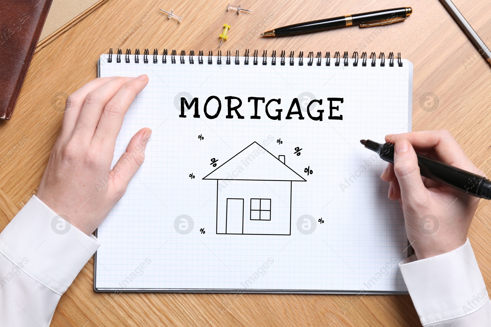 Image of Woman writing word Mortgage in notebook at wooden table, top view