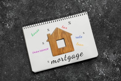 Image of Notebook with words and wooden house figure on dark table, top view