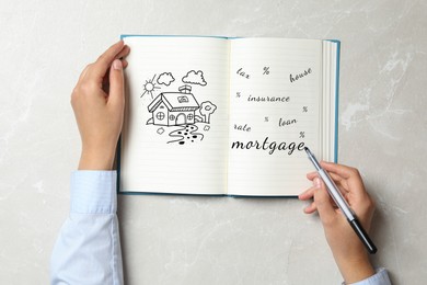 Woman writing word Mortgage in notebook at grey table, top view