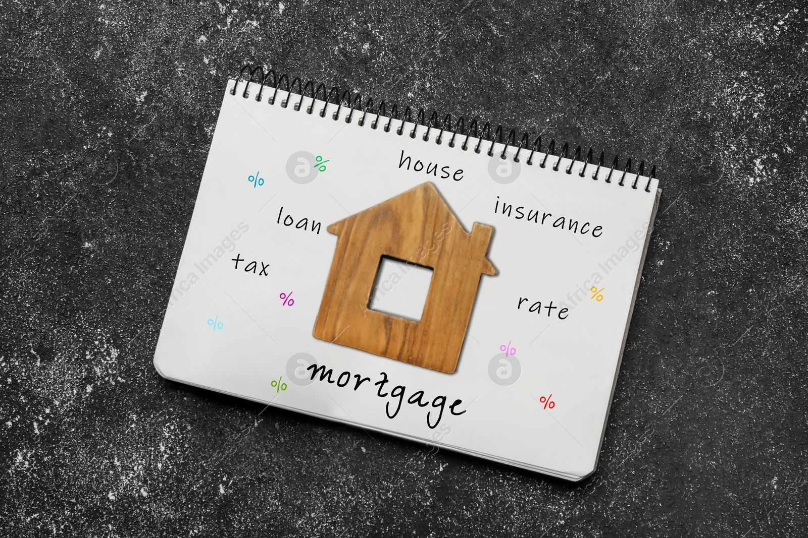 Image of Notebook with words and wooden house figure on dark table, top view