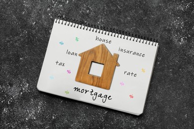 Notebook with words and wooden house figure on dark table, top view