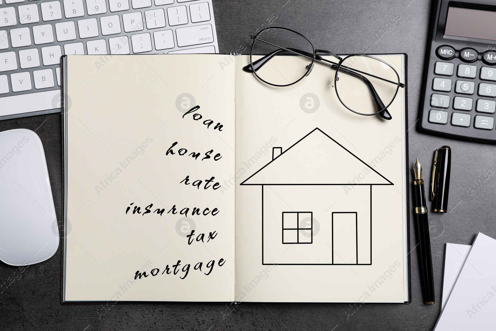 Image of Mortgage. Notebook with drawing of house and words on black table. Workplace with computer keyboard and mouse, top view