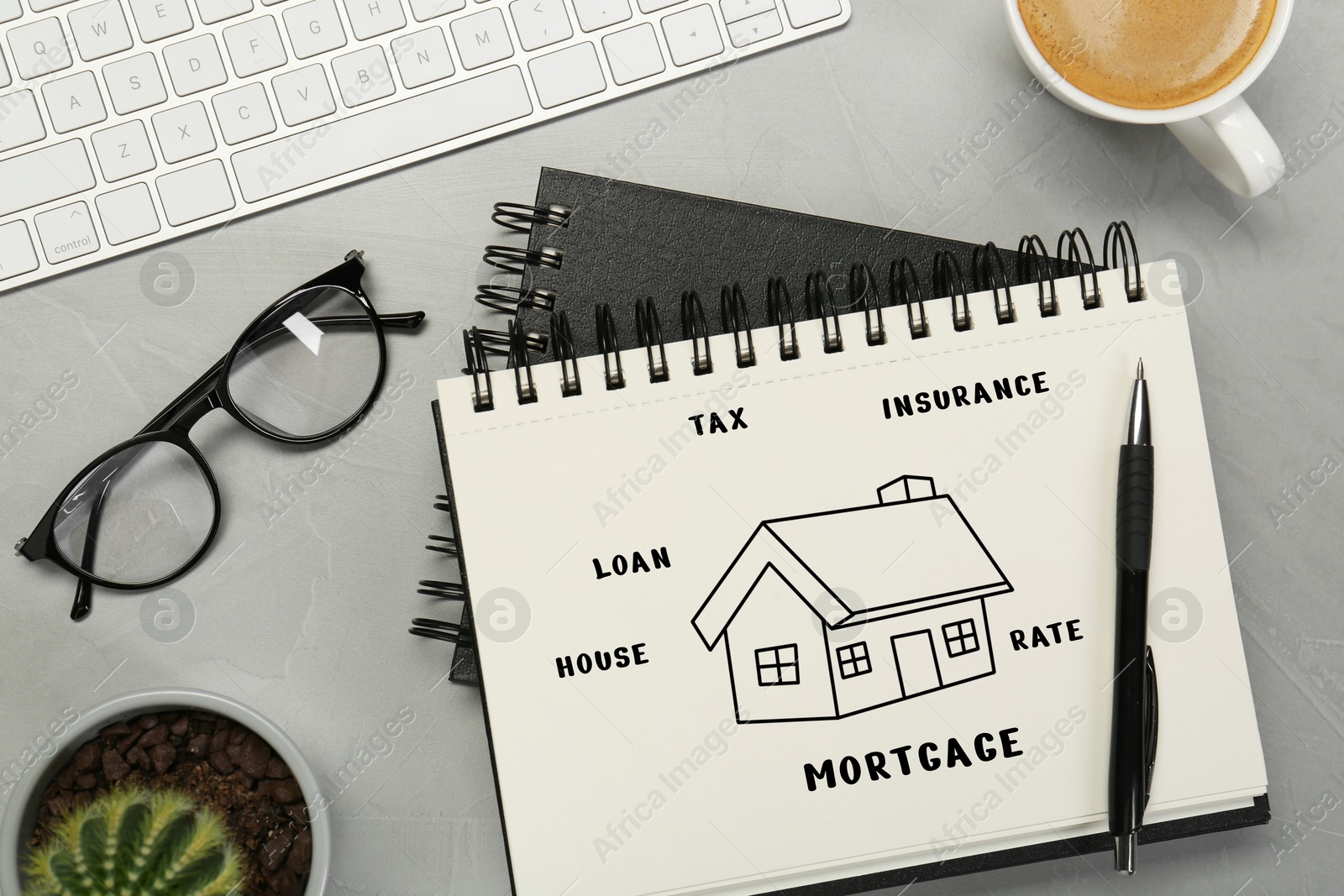 Image of Mortgage. Notebook with drawing of house and words on grey table. Workplace with computer keyboard, top view