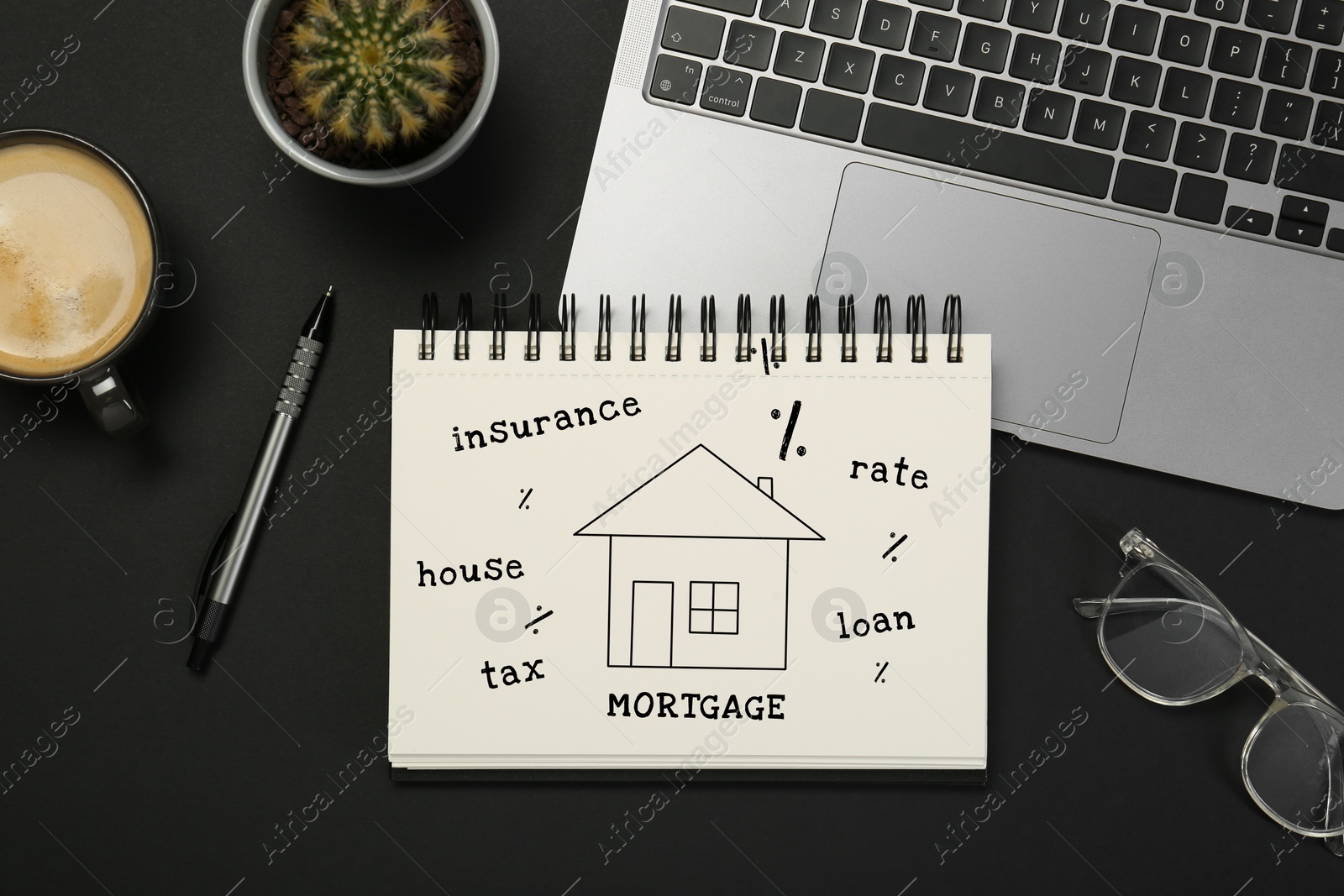 Image of Mortgage. Notebook with drawing of house, percent signs and words on black table. Workplace with laptop, top view