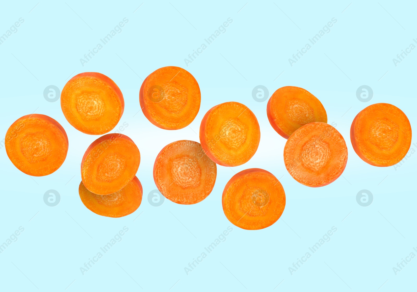 Image of Round carrot slices in air on light blue background