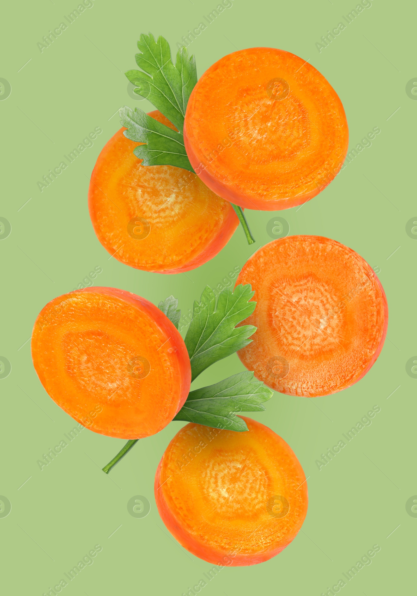 Image of Round carrot slices and parsley in air on pale green background