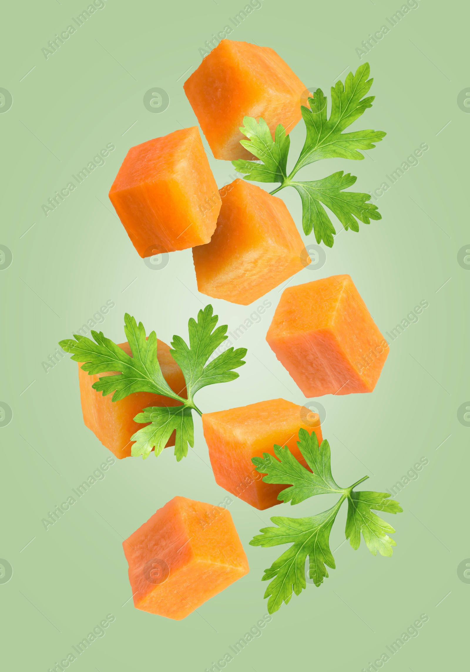 Image of Carrot cubes and parsley in air on pale green background