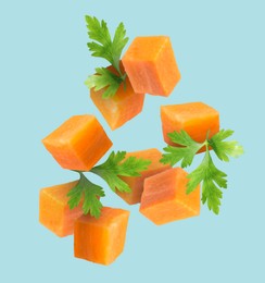 Image of Carrot cubes and parsley in air on light blue background