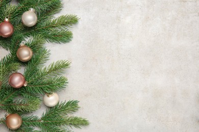 Photo of Christmas decor. Fir tree branches and shiny baubles on light textured table, flat lay. Space for text