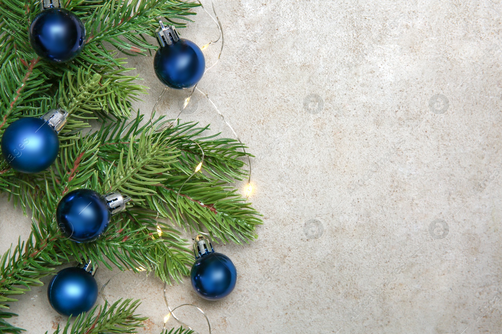 Photo of Christmas decor. Fir tree branches, festive lights and shiny baubles on light textured table, flat lay. Space for text