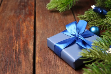 Photo of Fir tree branches with Christmas decor and gift box on wooden table, closeup. Space for text