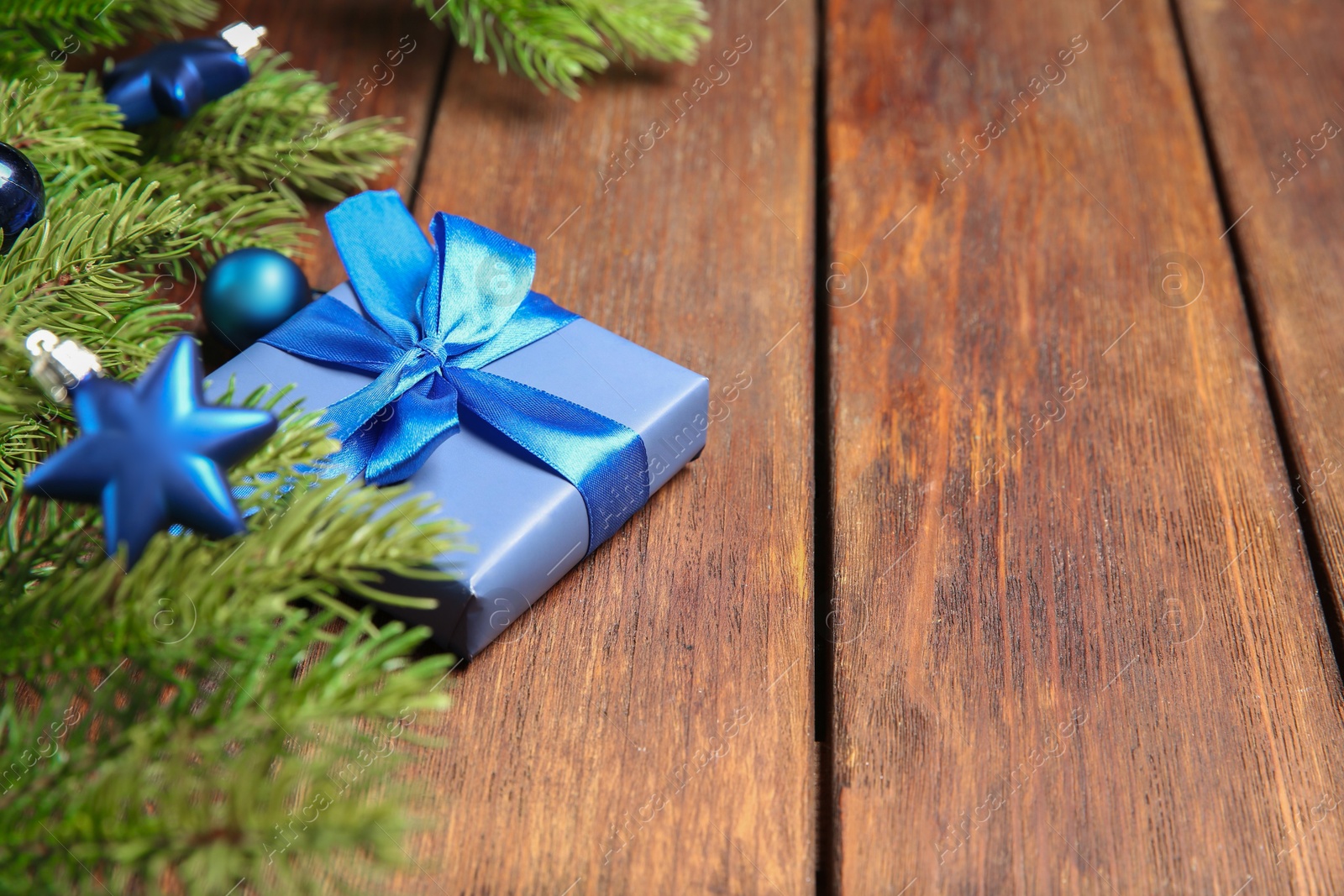 Photo of Fir tree branches with Christmas decor and gift box on wooden table, closeup. Space for text