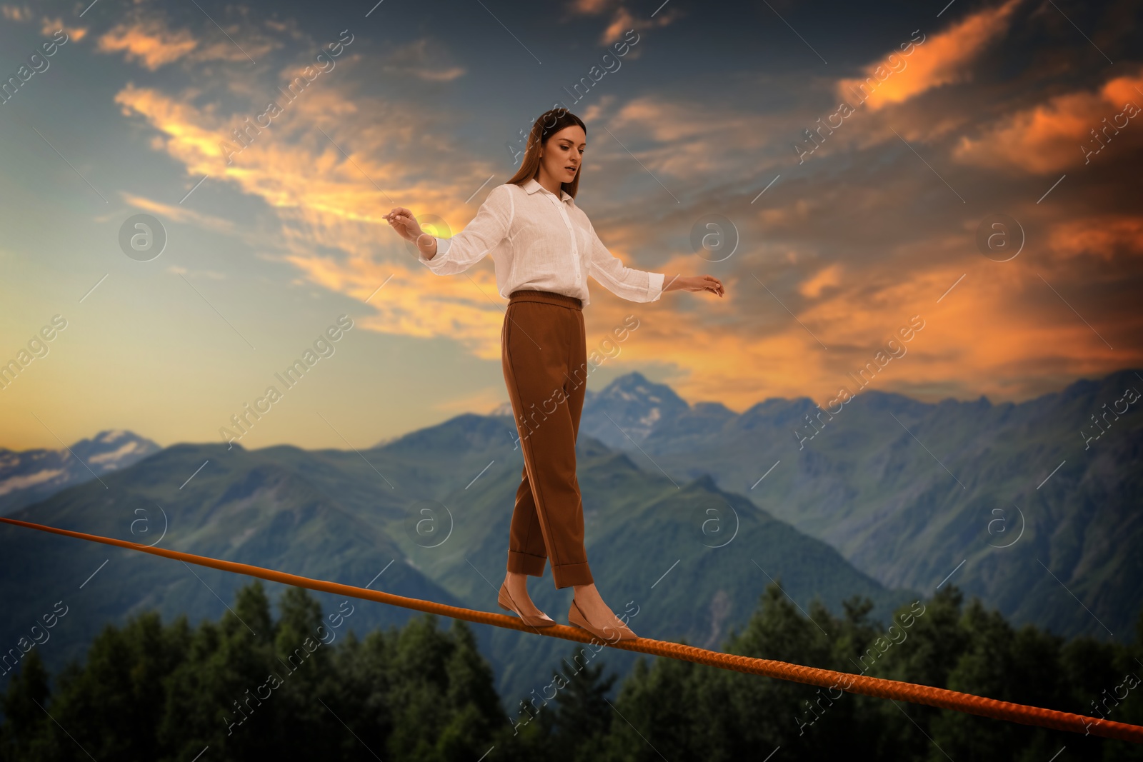 Image of Businesswoman walking rope in mountains. Concept of risk and balance