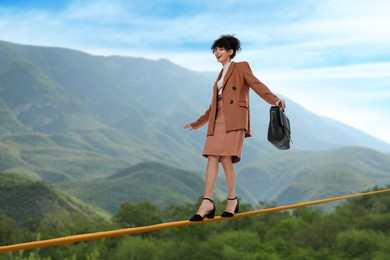 Image of Businesswoman walking rope in mountains. Concept of risk and balance