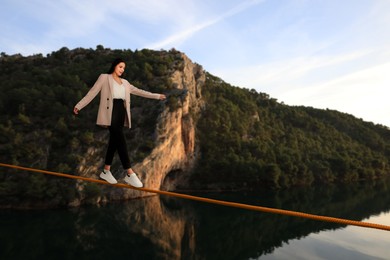 Image of Businesswoman walking rope in mountains. Concept of risk and balance