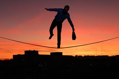 Businessman walking rope over city at sunset. Concept of risk and balance