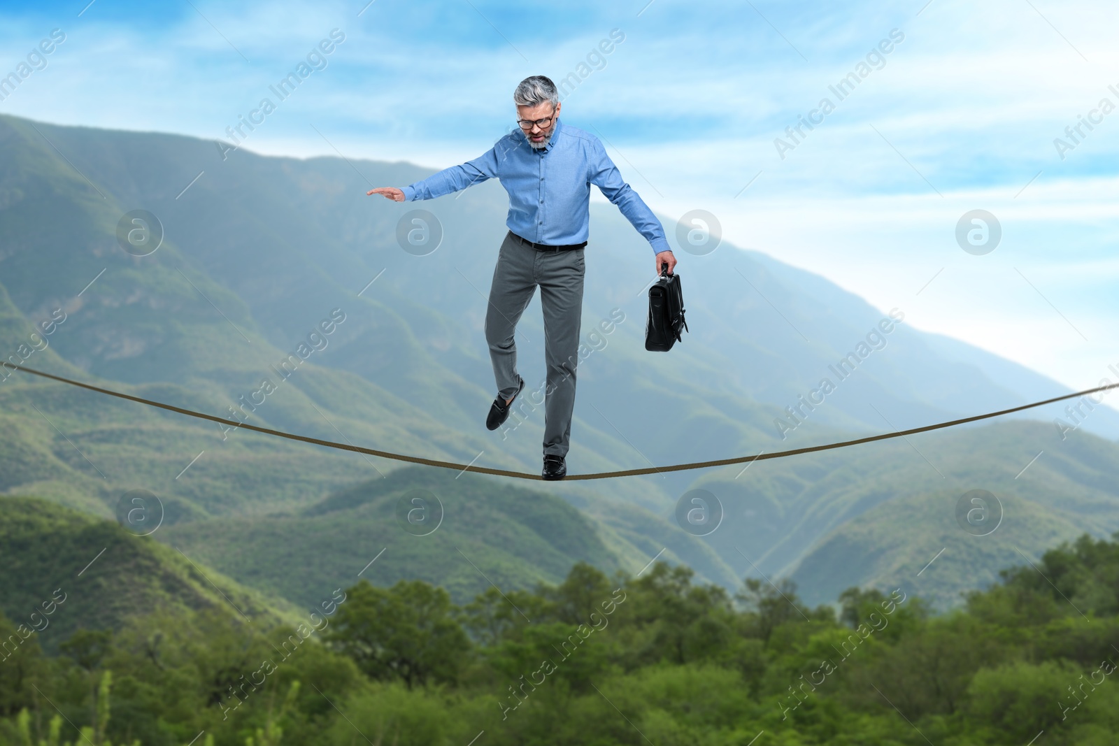 Image of Businessman walking rope in mountains. Concept of risk and balance