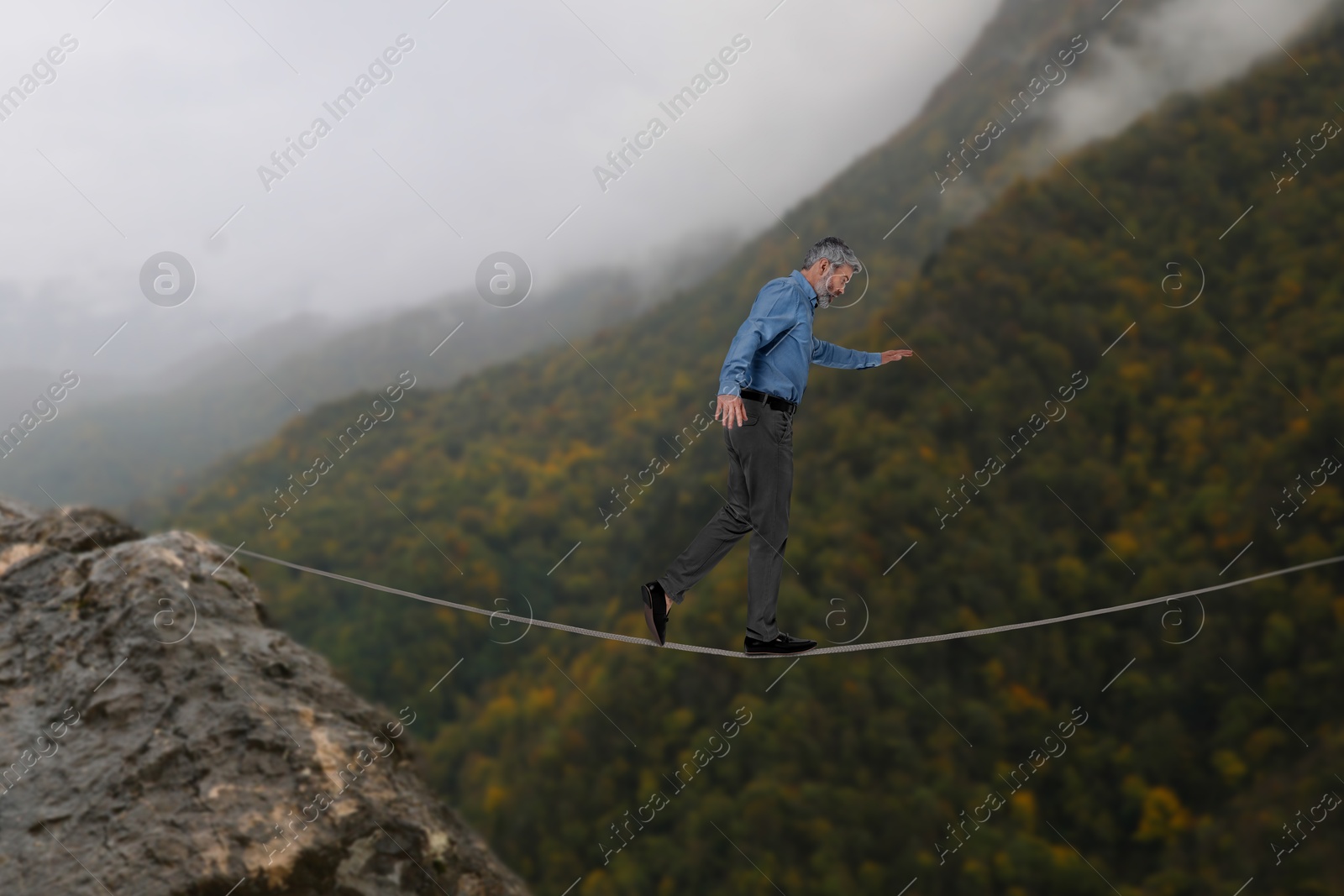 Image of Businessman walking rope in mountains. Concept of risk and balance