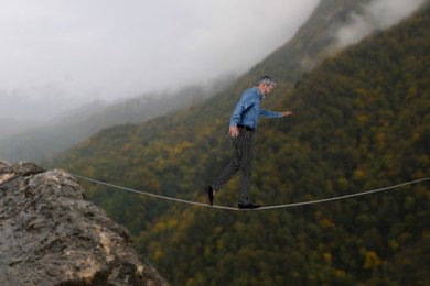 Businessman walking rope in mountains. Concept of risk and balance