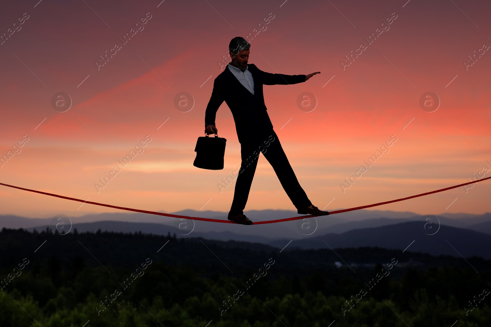 Image of Businessman walking rope in mountains at sunset. Concept of risk and balance