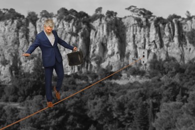 Image of Businessman walking rope in mountains. Concept of risk and balance