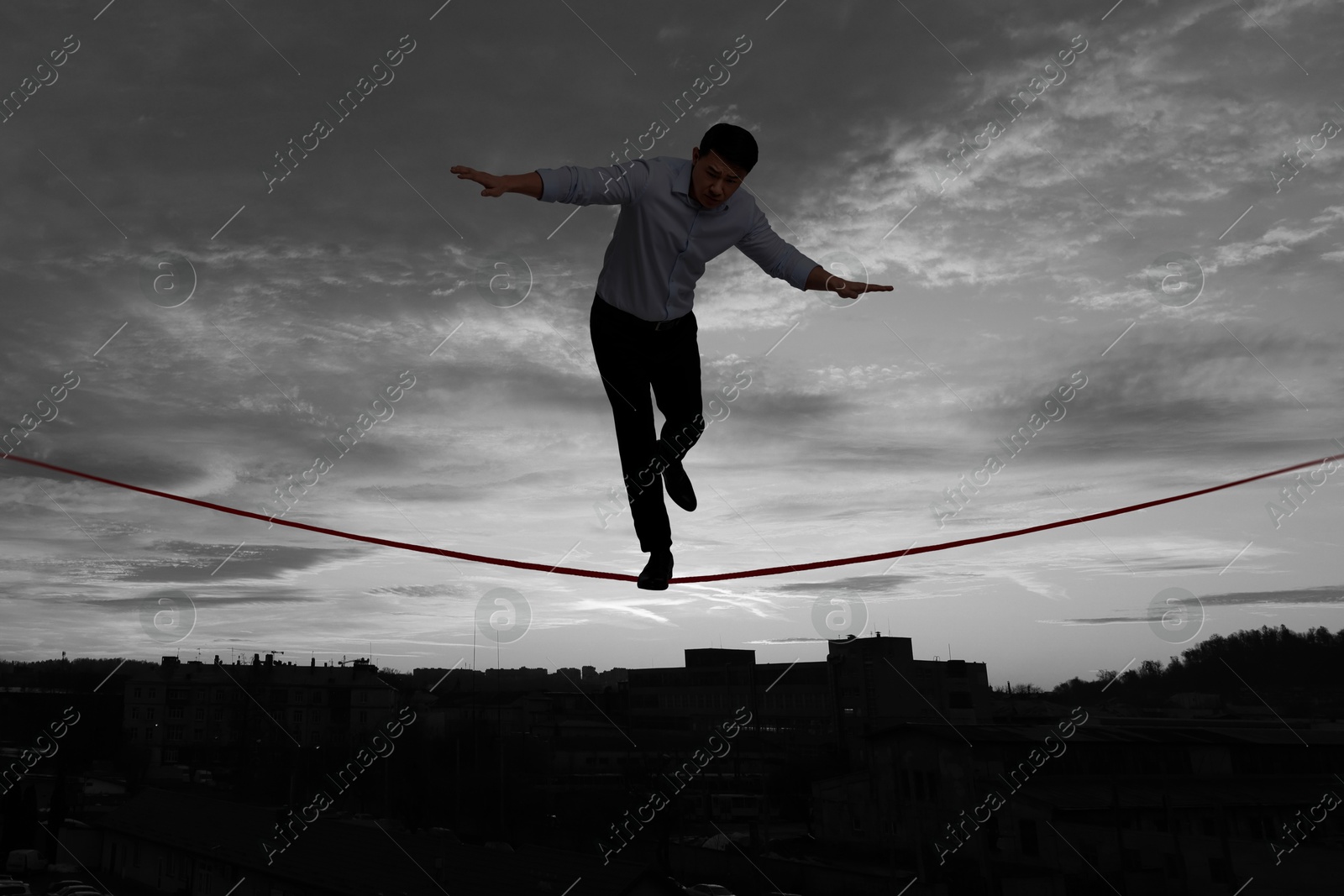 Image of Businessman walking rope over city at sunset. Concept of risk and balance