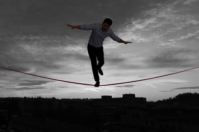 Image of Businessman walking rope over city at sunset. Concept of risk and balance