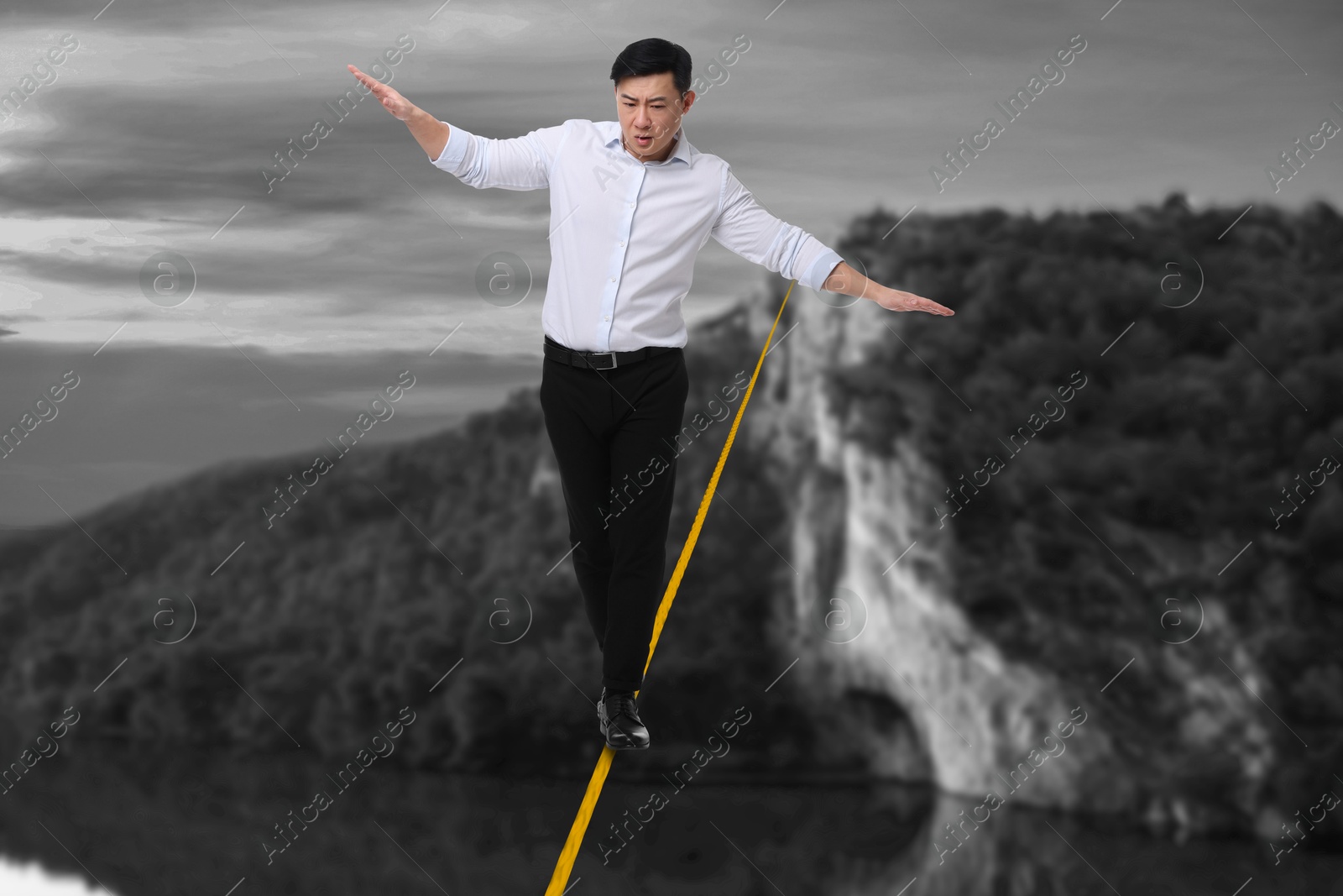 Image of Businessman walking rope in mountains. Concept of risk and balance