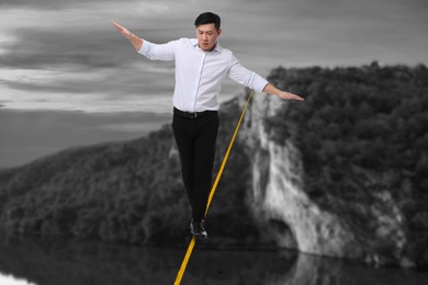 Image of Businessman walking rope in mountains. Concept of risk and balance