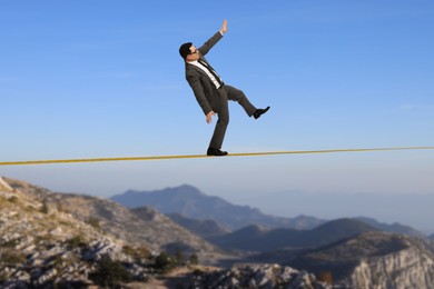 Businessman walking rope in mountains. Concept of risk and balance