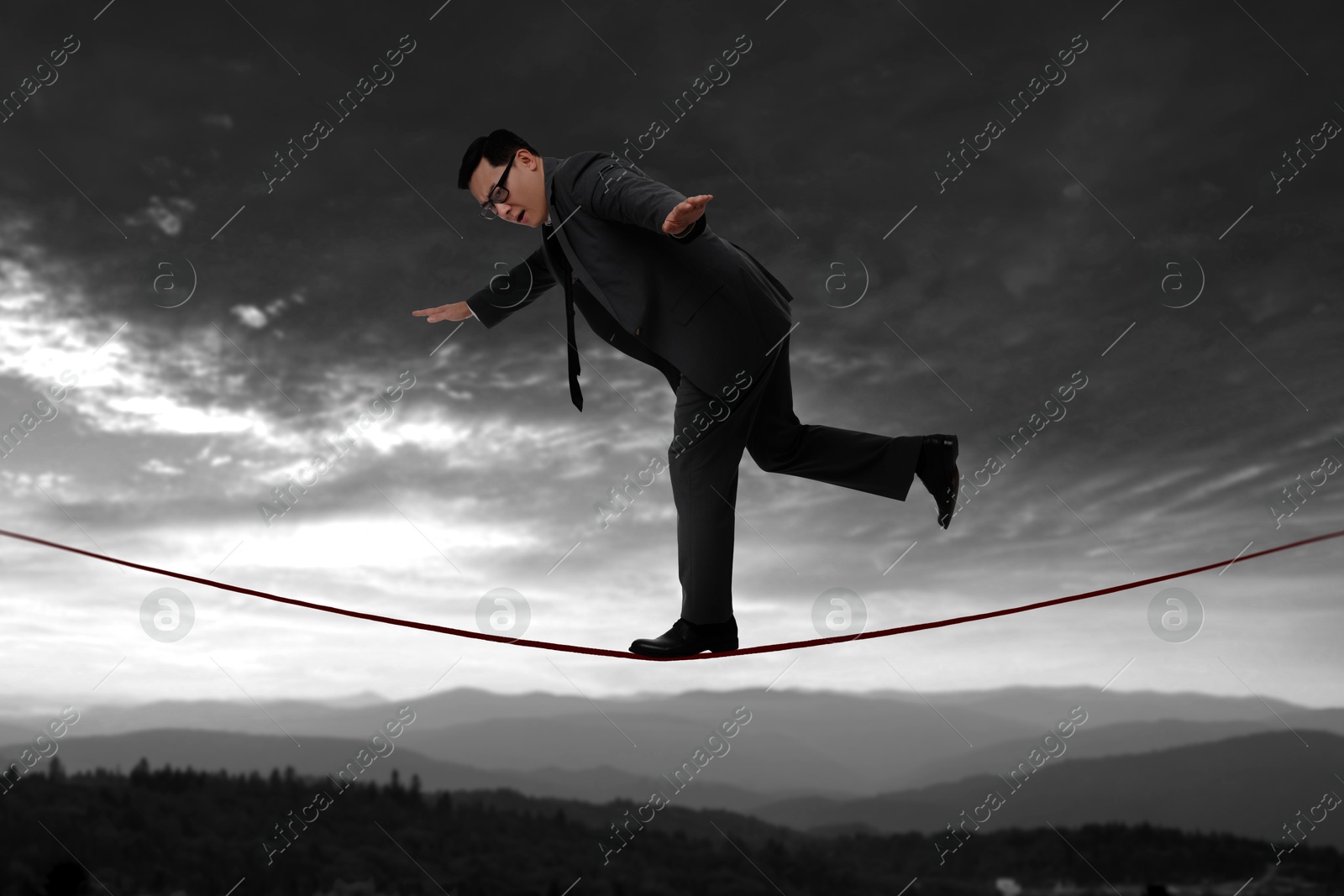 Image of Businessman walking rope in mountains. Concept of risk and balance