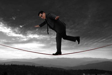 Businessman walking rope in mountains. Concept of risk and balance