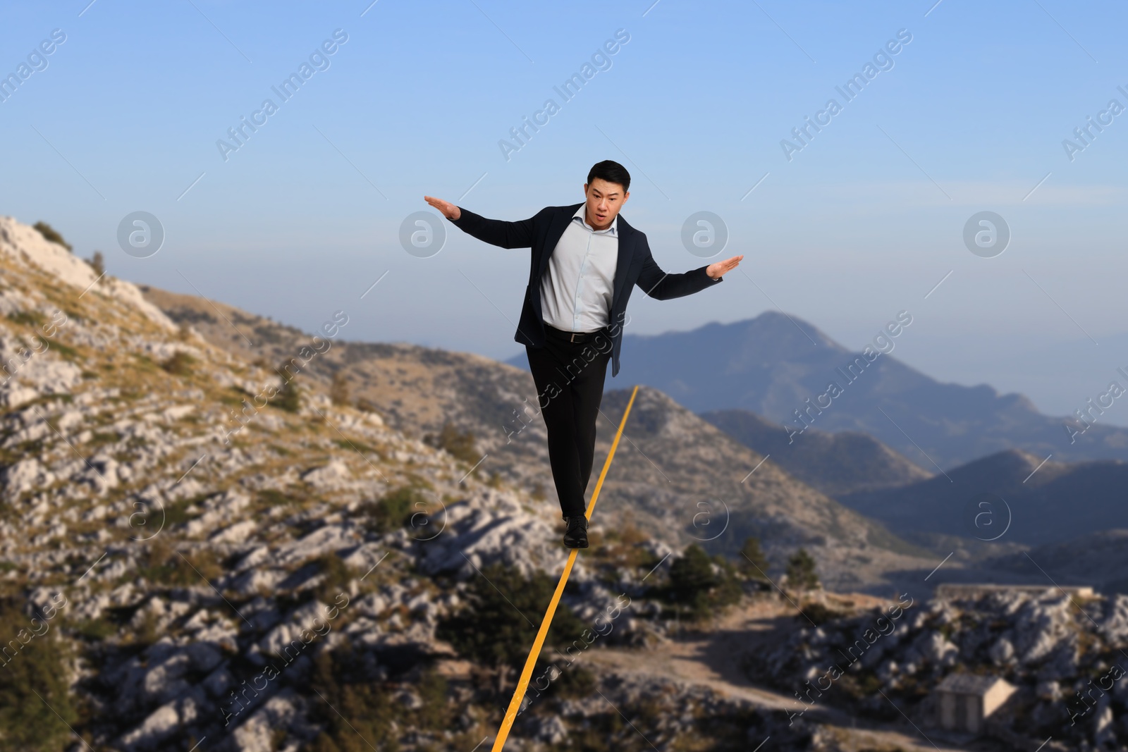 Image of Businessman walking rope in mountains. Concept of risk and balance