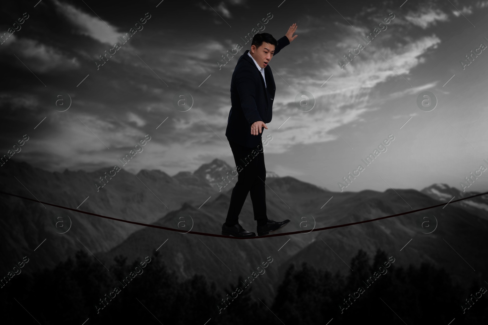 Image of Businessman walking rope in mountains. Concept of risk and balance