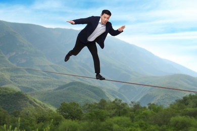 Image of Businessman walking rope in mountains. Concept of risk and balance