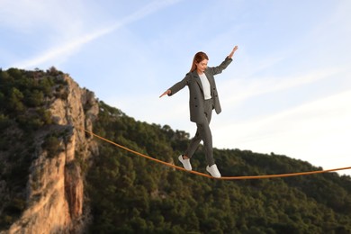 Businesswoman walking rope in mountains. Concept of risk and balance