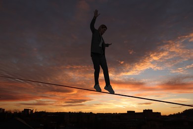 Businesswoman walking rope over city at sunset. Concept of risk and balance